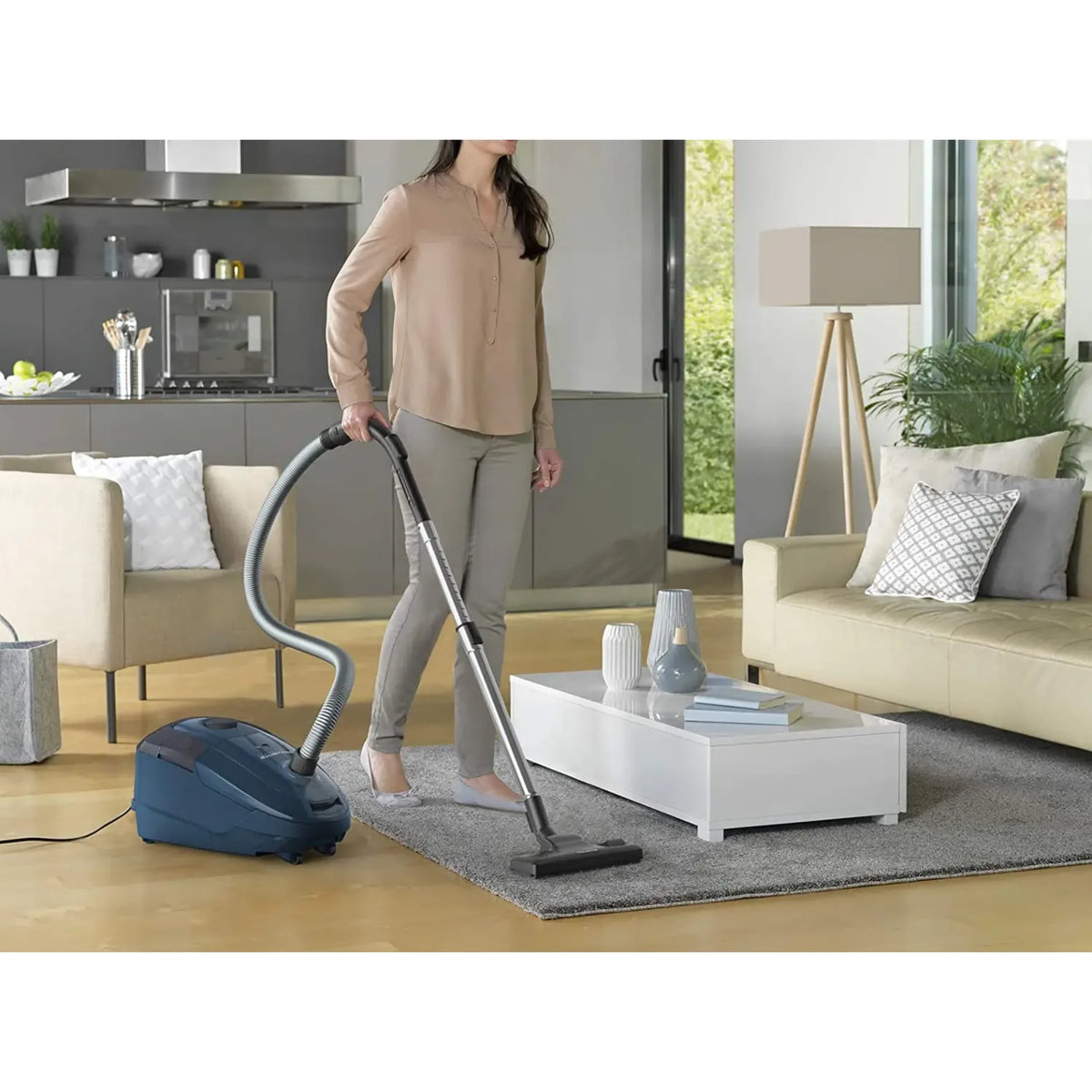 Rowenta RO3125 in Blue, woman vacuuming a rug beside a kitchen and sofa