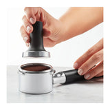 KitchenAid Artisan 5KES6503B Espresso Machine in Candy Apple, hands pressing ground coffee in the portafilter with a tamper