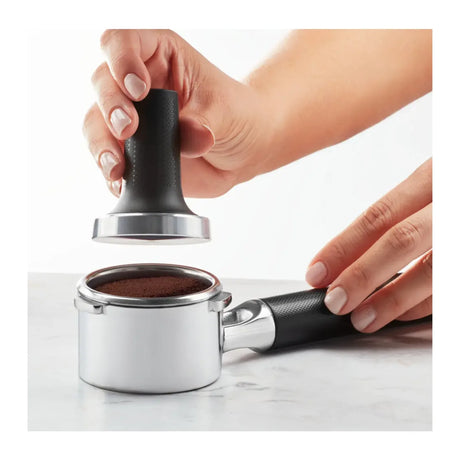 KitchenAid Artisan 5KES6503B Espresso Machine in Candy Apple, hands pressing ground coffee in the portafilter with a tamper
