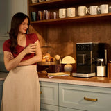 KitchenAid 5KES8454 in Matte Black, on a kitchen worktop beside a woman holding a cup
