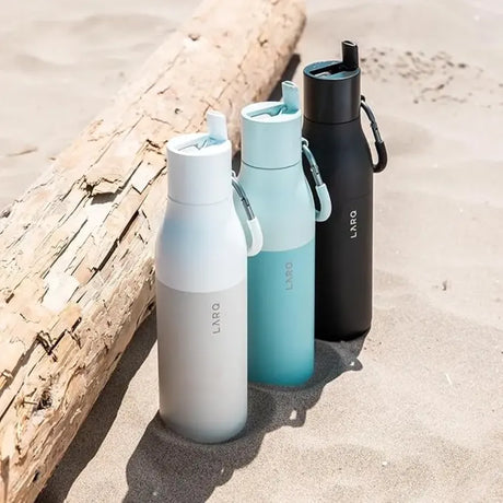 LARQ BNSOB074A, three bottles in different colours standing in sand by a log